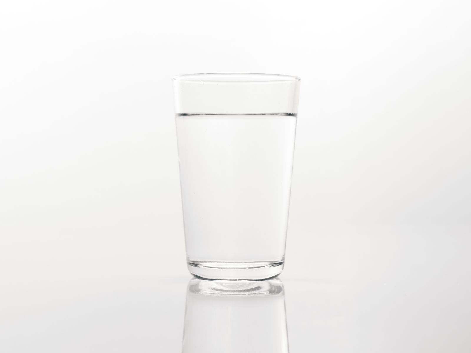Close-up of a clear glass of water on a reflective white surface