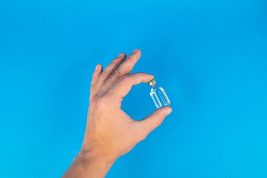 Hand holding a small clear glass vial against a bright background
