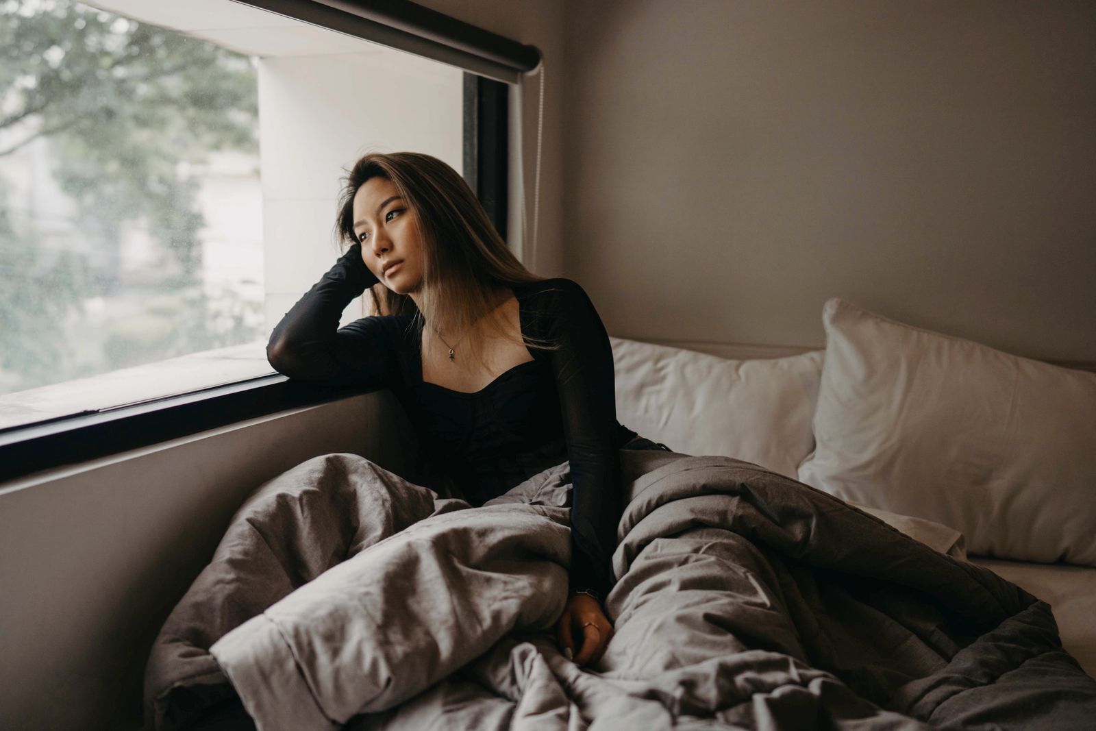 Woman wrapped in a blanket sitting quietly beside a window in a bright room