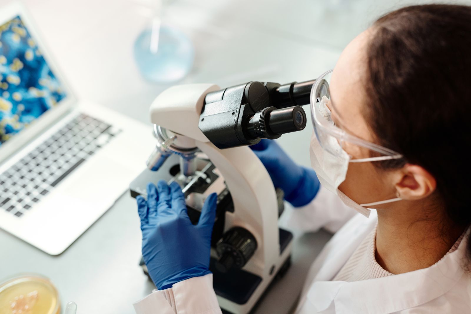 Scientist in protective gear examining a sample through a microscope