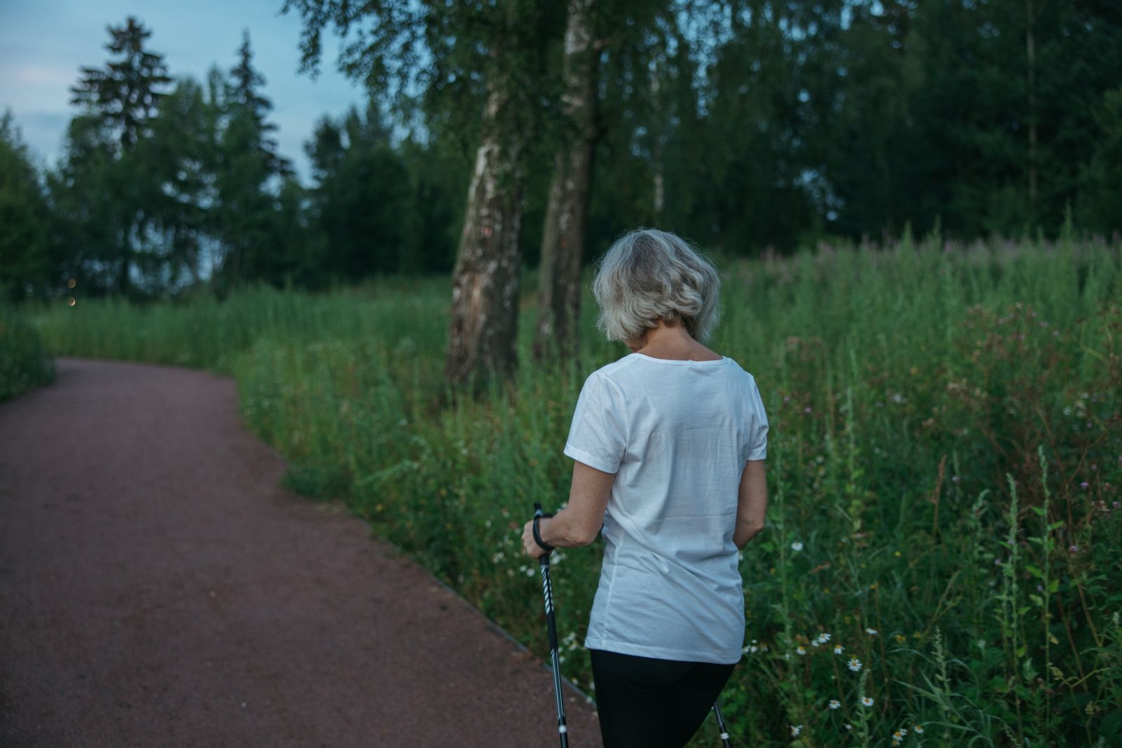 Woman using Nordic walking poles on a tree-lined park trail