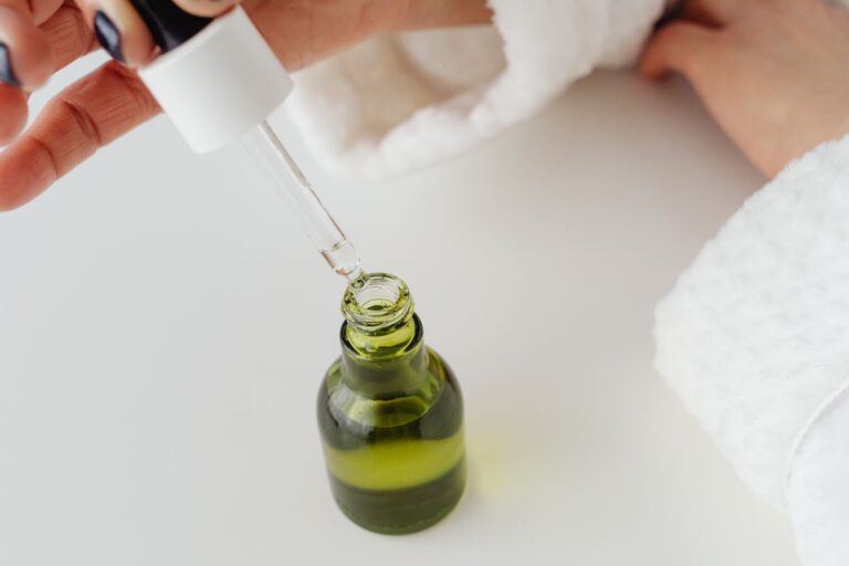 Hands holding a glass dropper above a serum bottle