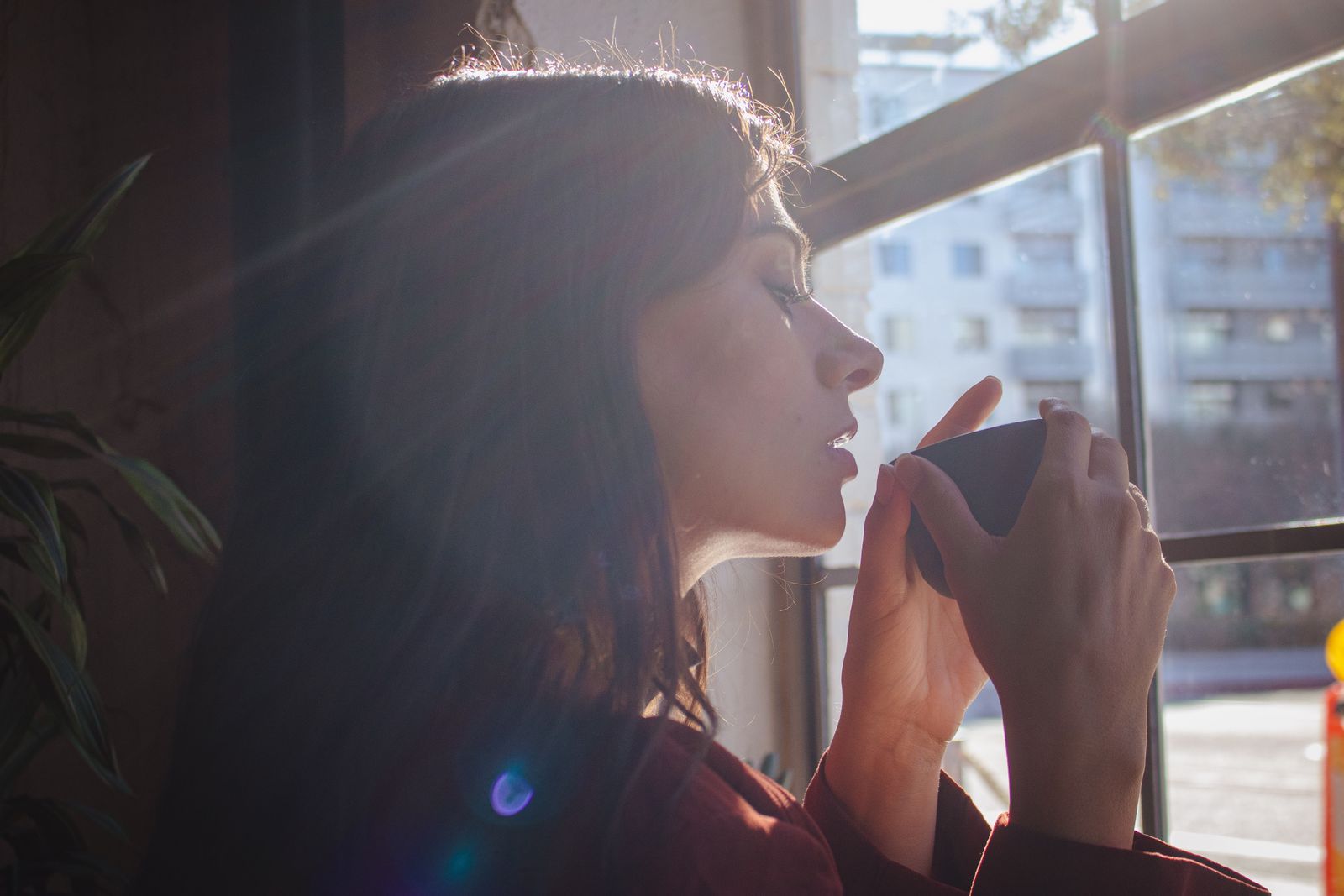 Woman holding a warm drink beside a sunlit window