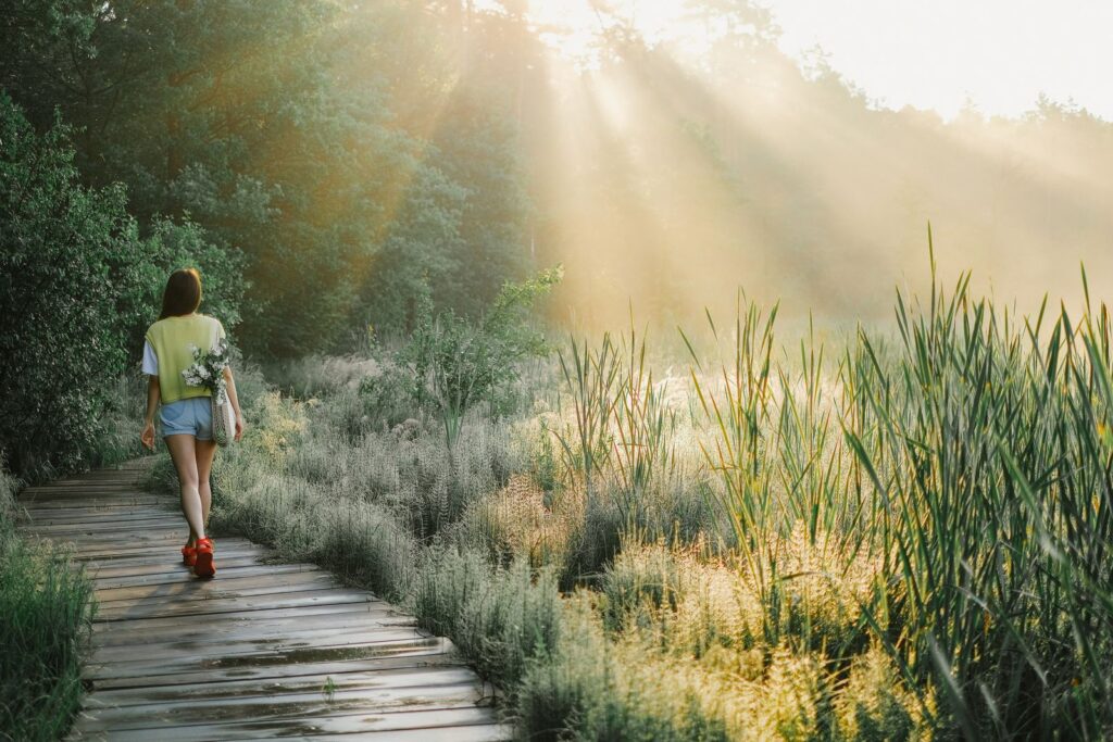 Woman walking on a wooden path through a sunlit forest