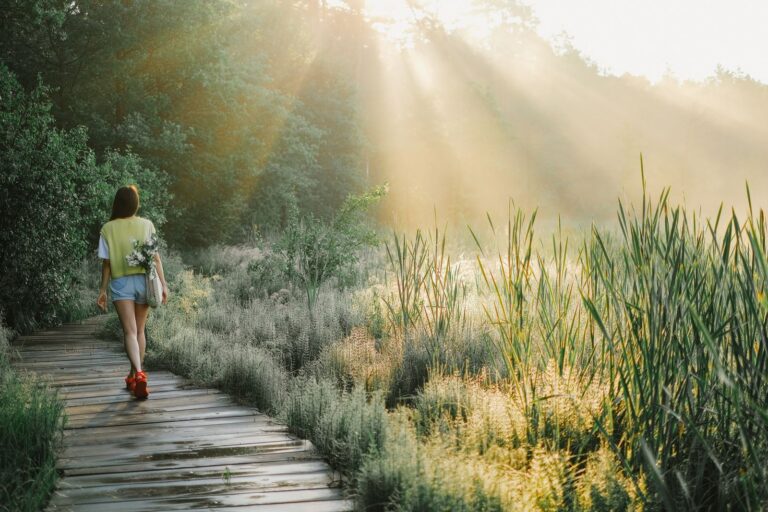 Woman walking on a wooden path through a sunlit forest