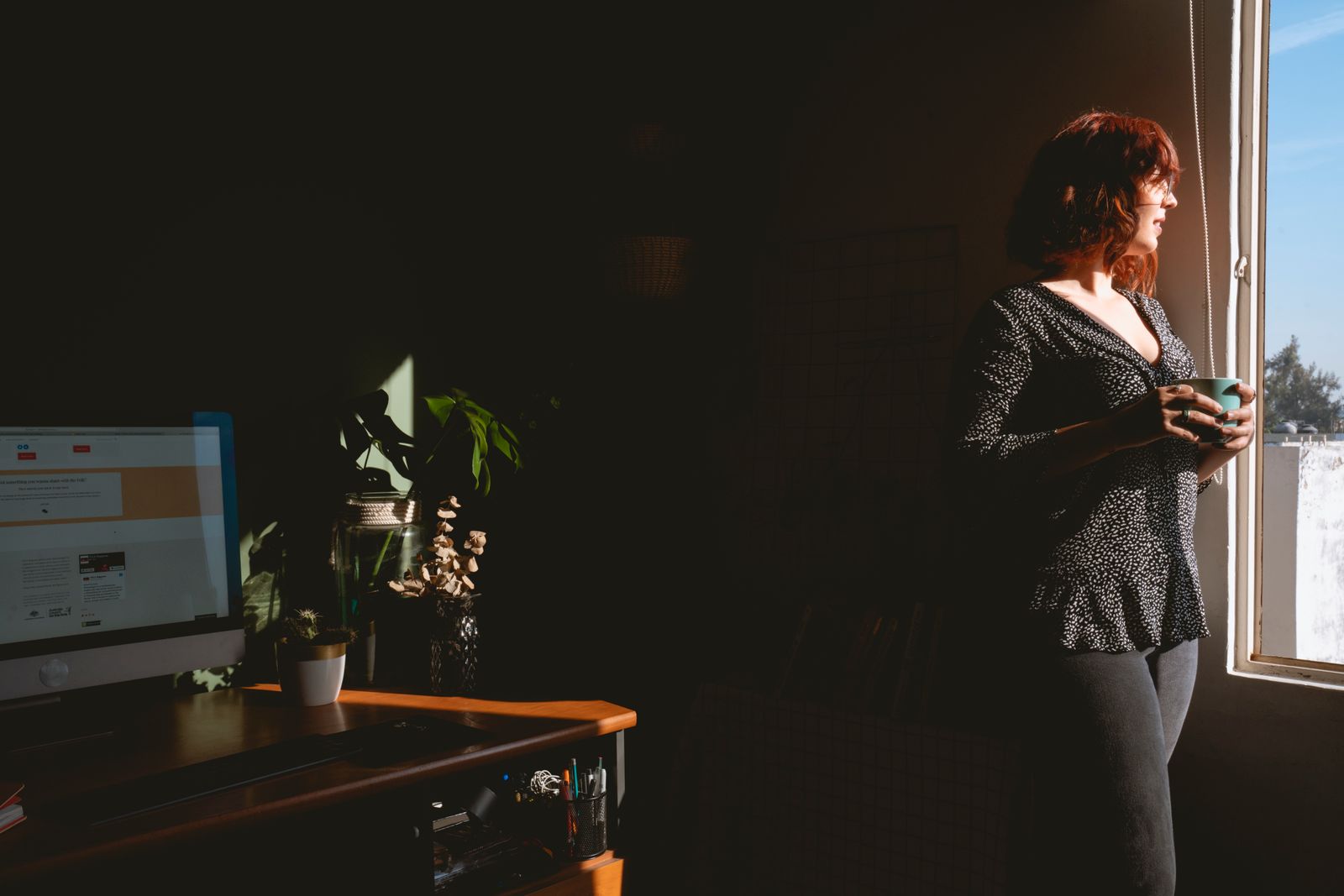 Woman standing in a home office holding a mug in bright natural light