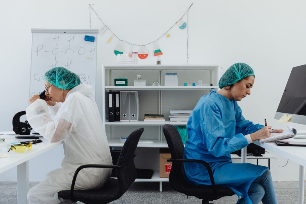 Two scientists working together, one at a microscope and one recording results