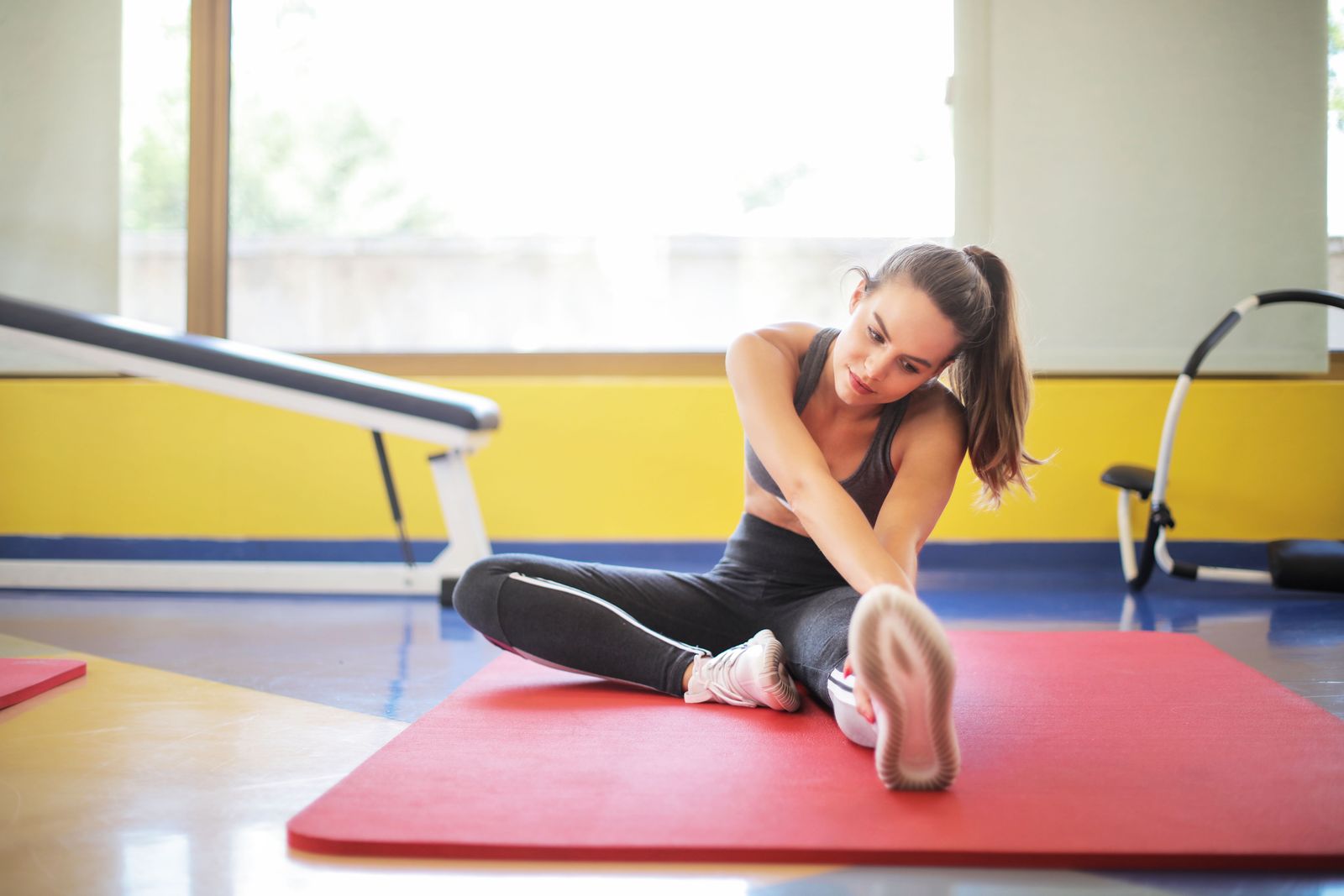 Woman stretching on a red exercise mat in a bright indoor space