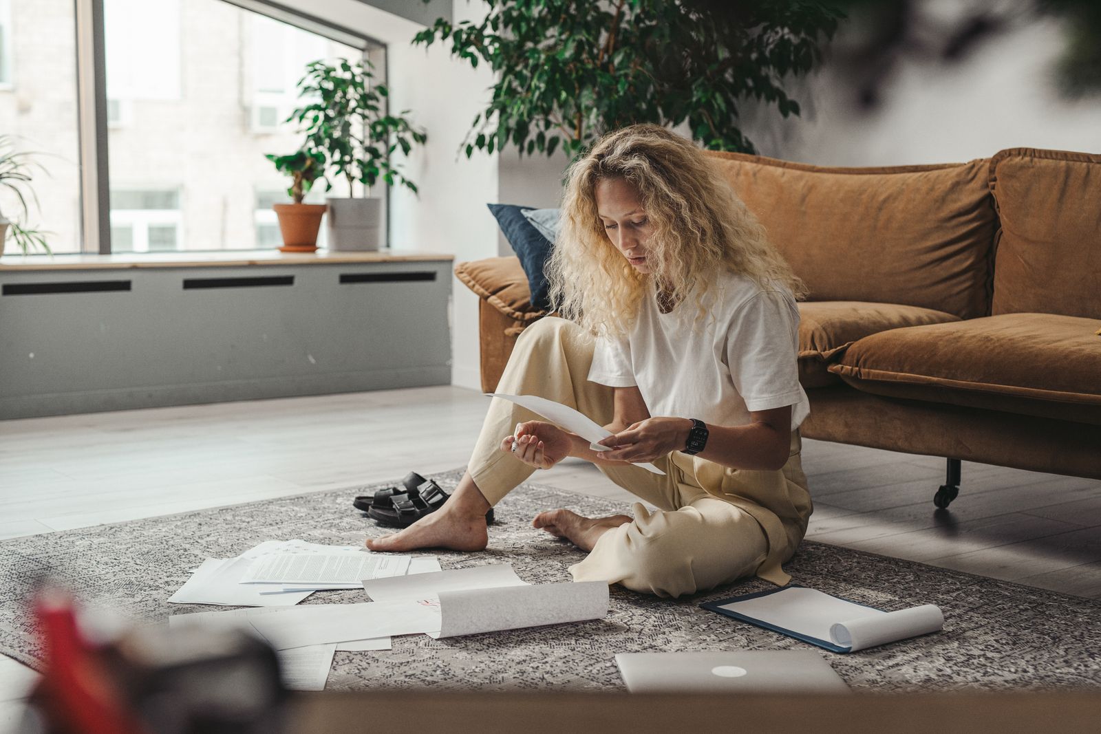 Woman sitting on the floor at home reading through printed research papers