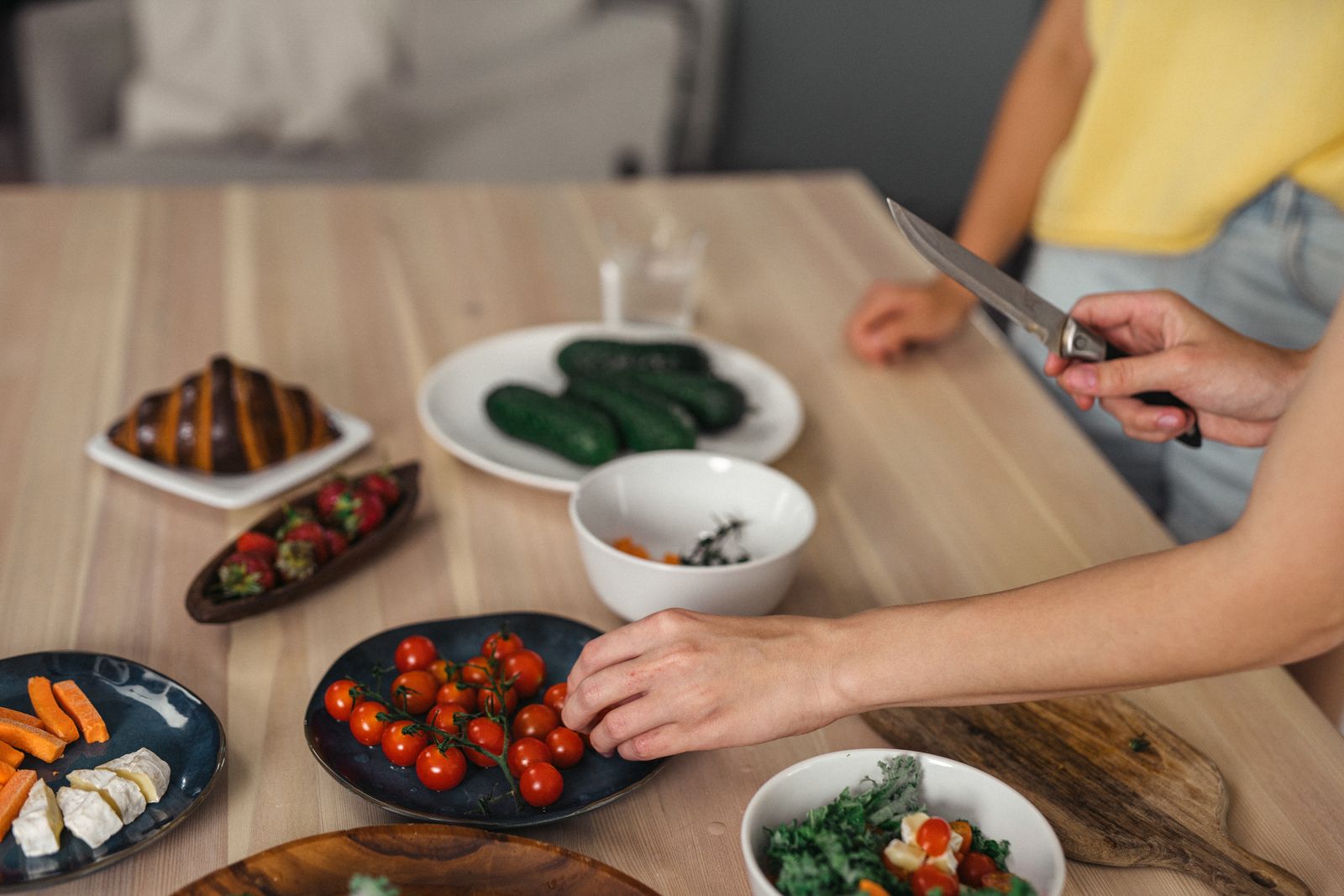 Hands slicing fresh vegetables and fruit on a wooden kitchen table