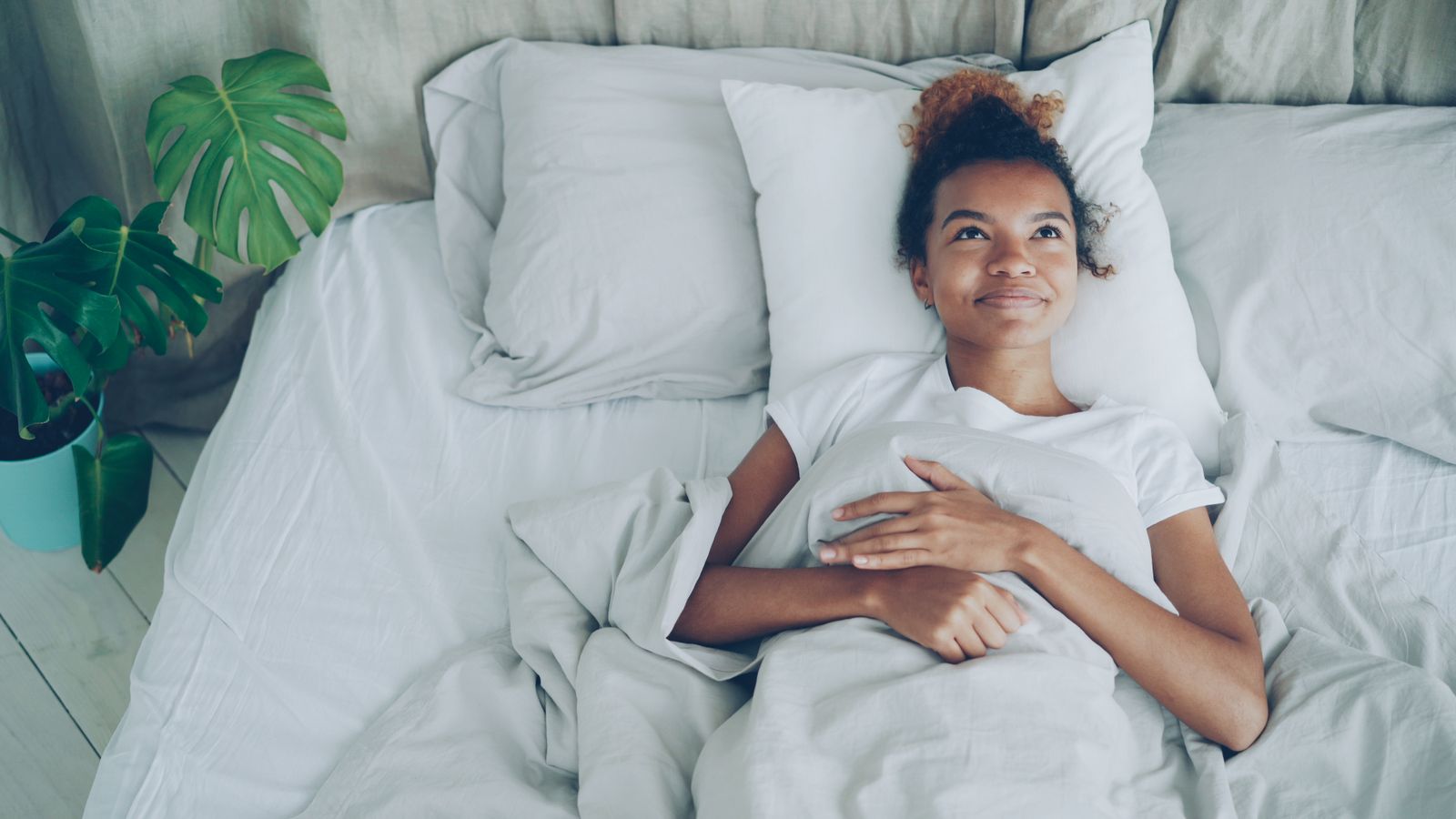 A woman relaxing in bed beside a large houseplant