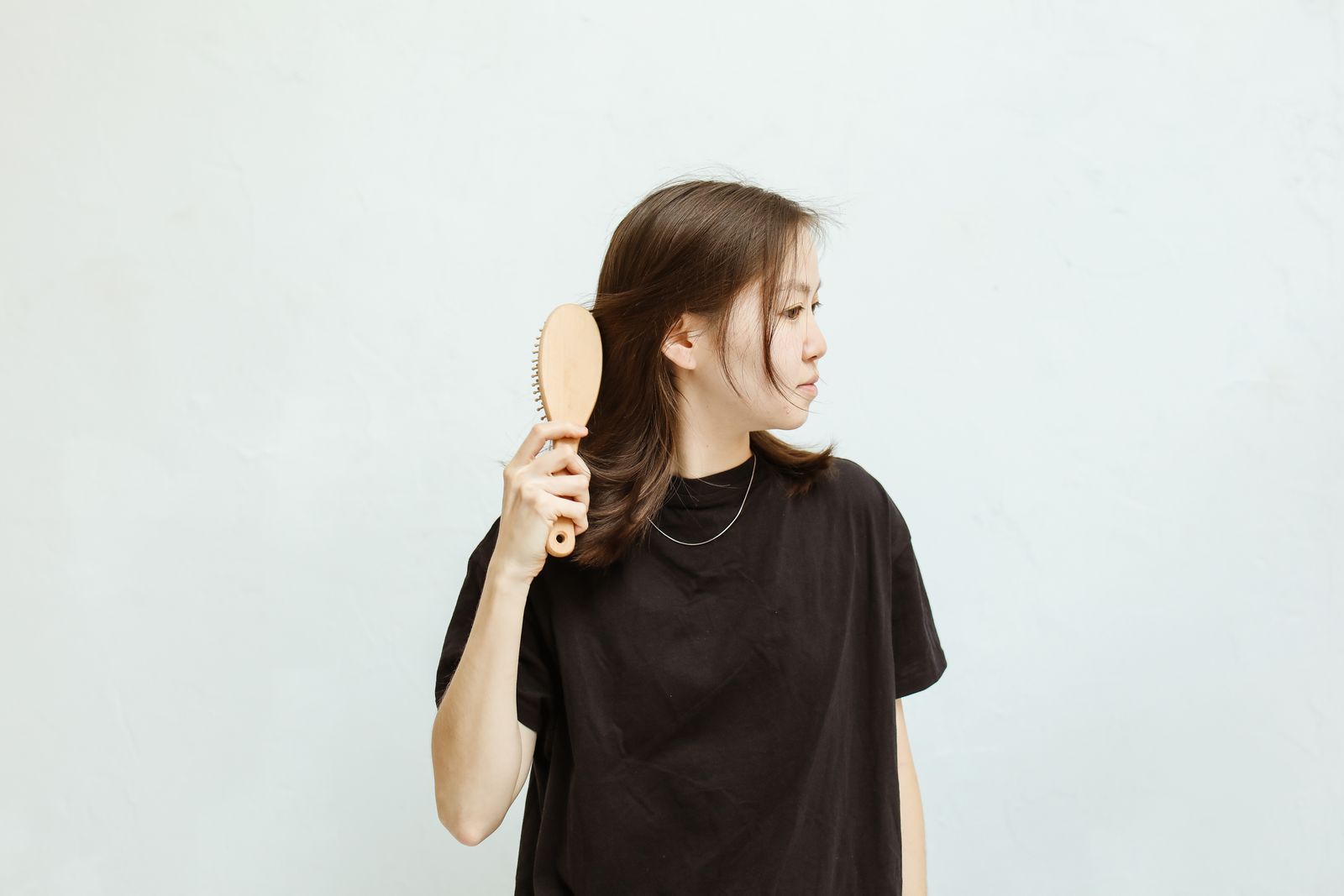 A woman combing her hair against a plain background
