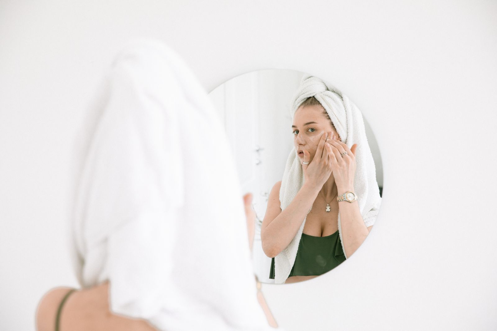 A woman applying face cream reflected in a bathroom mirror