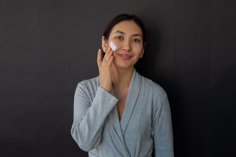 A woman in a bathrobe applying moisturiser to her cheek