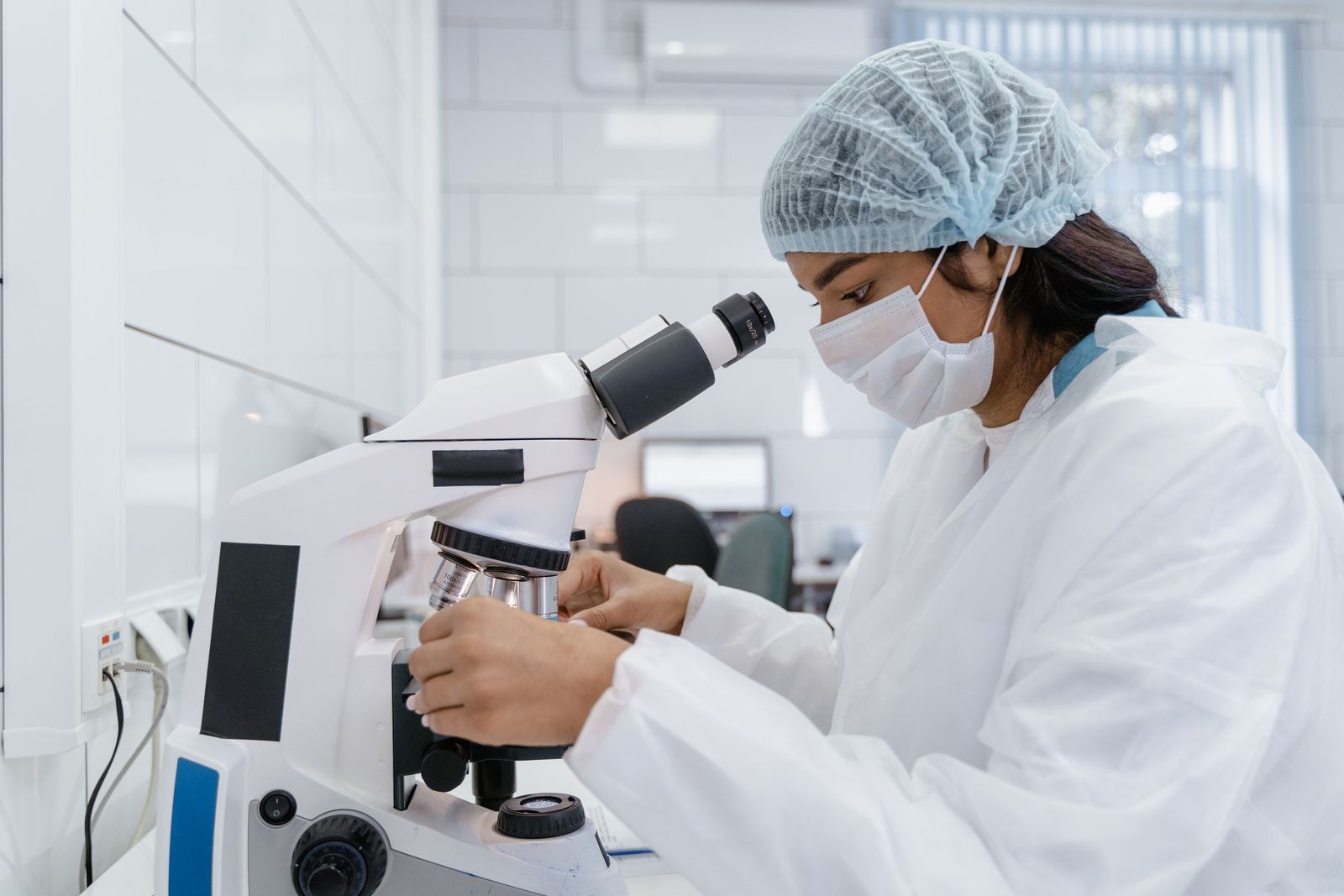 A female scientist in protective gear analysing samples under a microscope