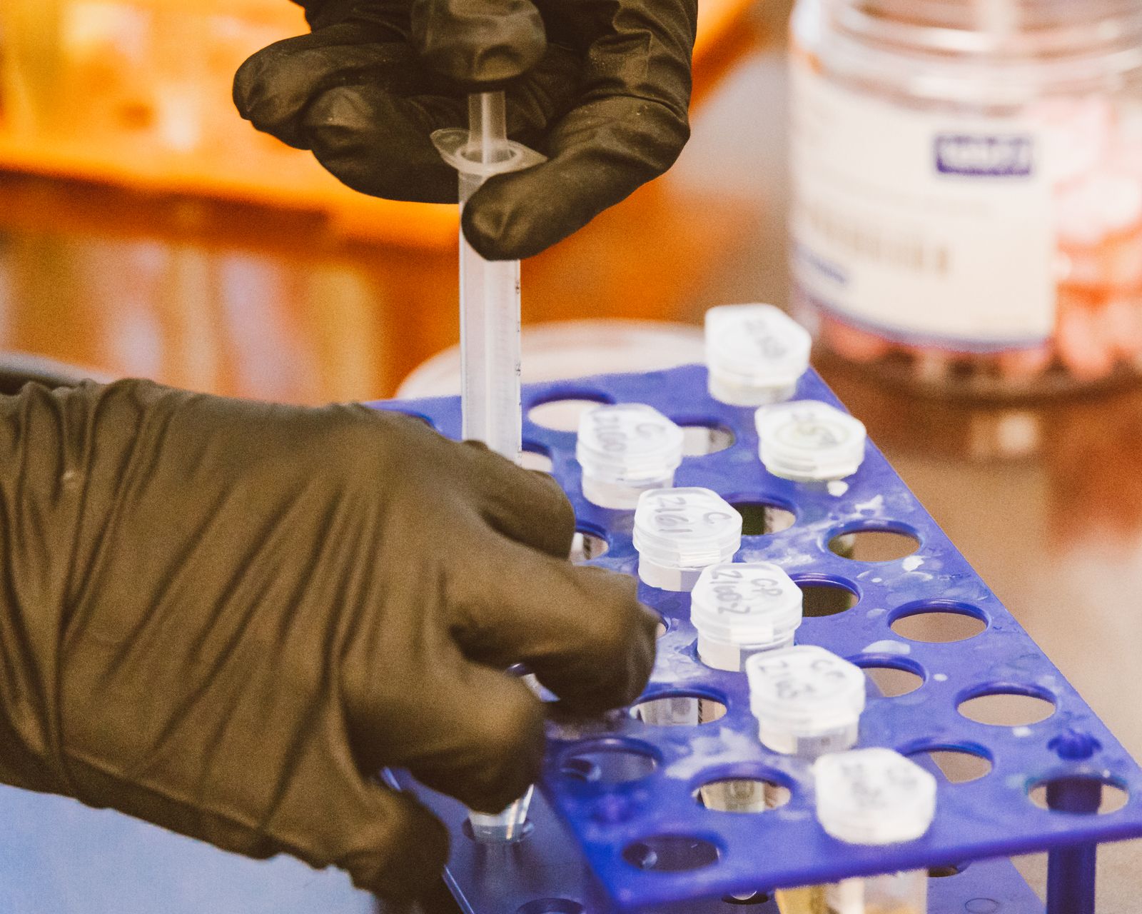 Gloved hands using a syringe for precise measurement in a laboratory