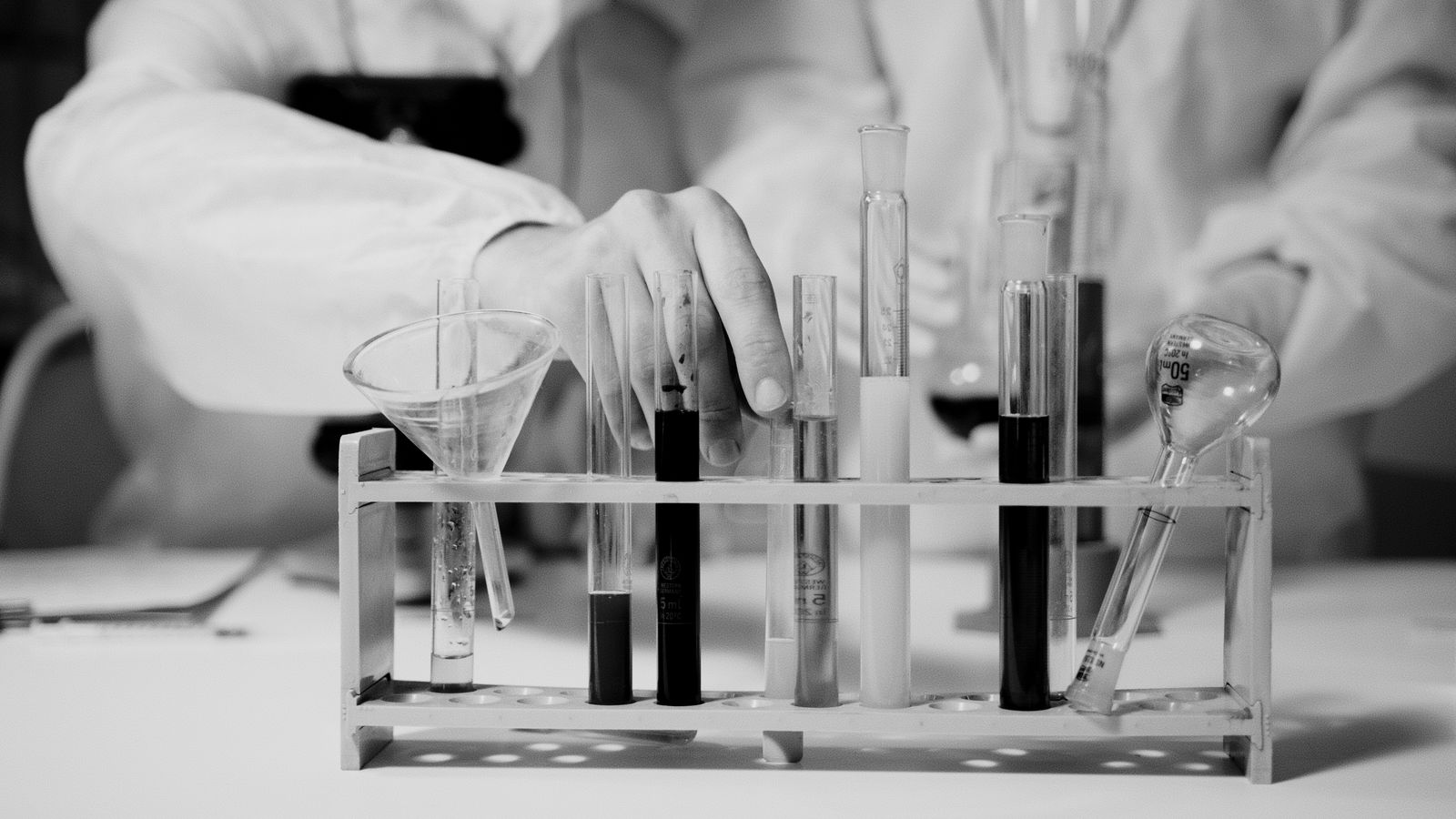 A gloved hand handling test tubes during a laboratory experiment