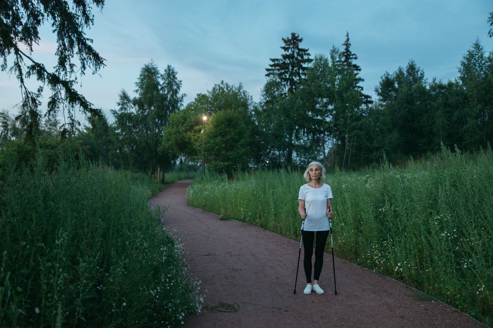 An older woman using Nordic walking poles in a green space