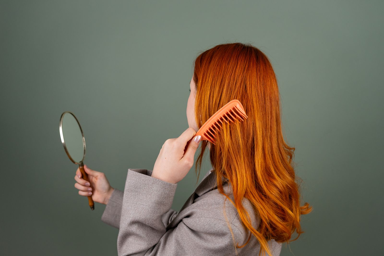 A woman with red hair combing it while holding a mirror