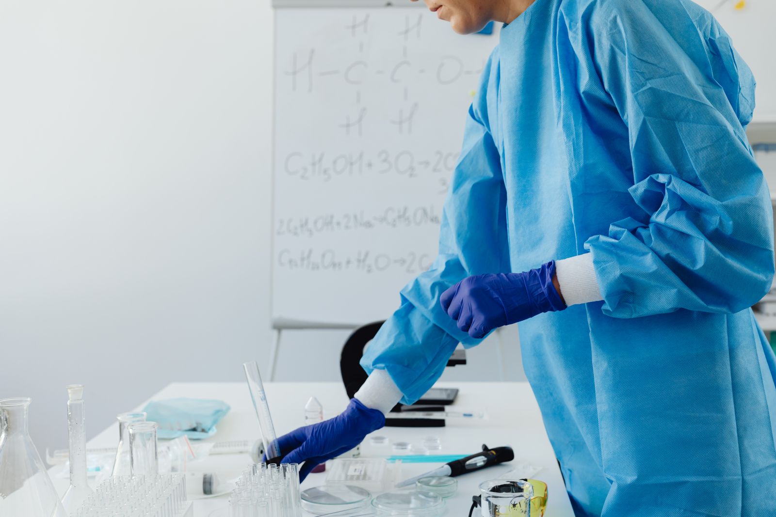A researcher in protective clothing working with chemical formulas