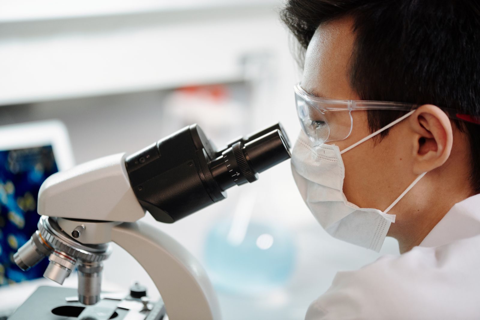 A researcher in goggles and mask examining samples through a microscope