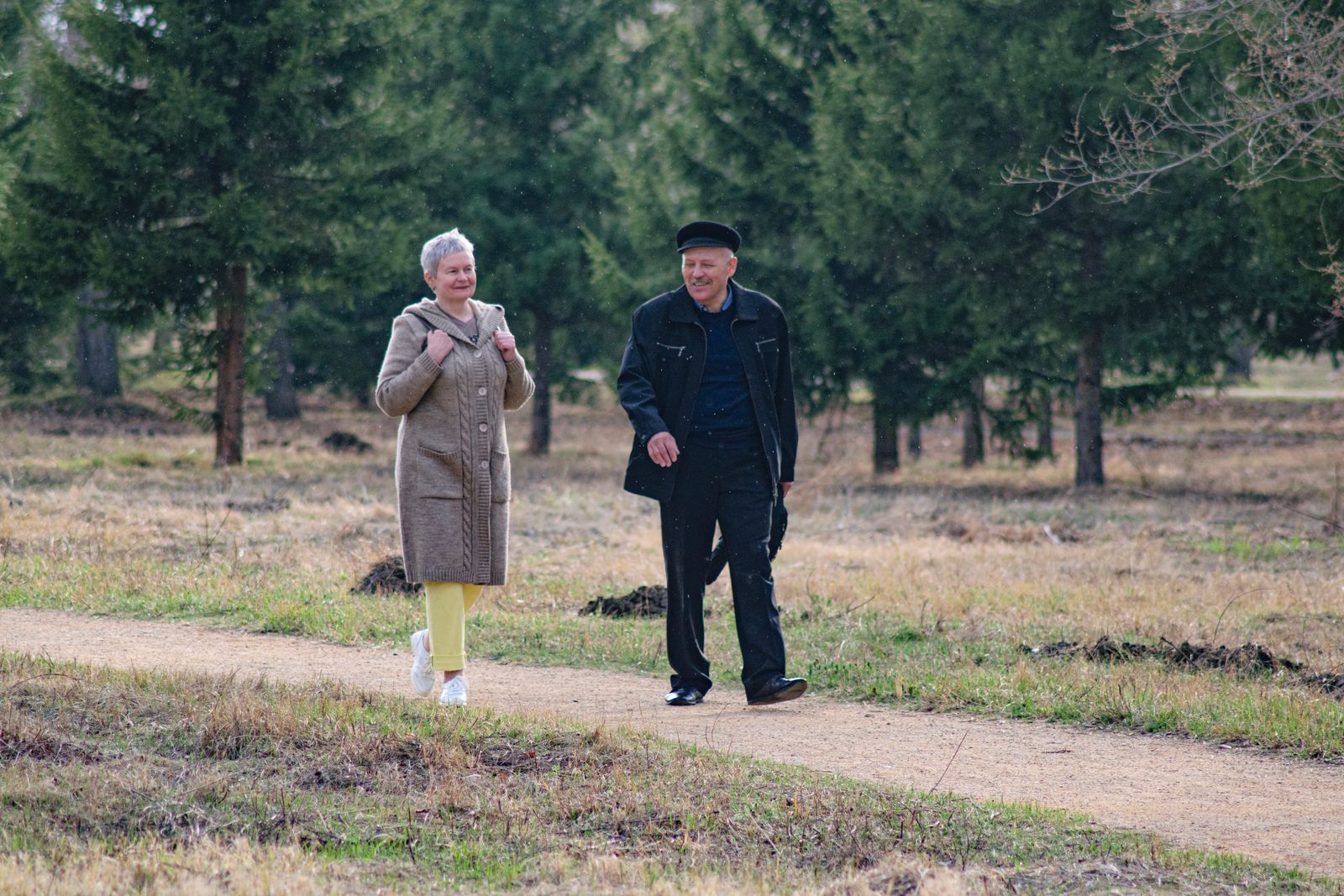 Two older people walking along a park path in spring