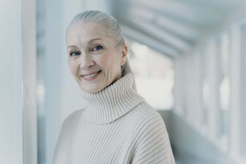 A woman with grey hair smiling in a calm indoor setting