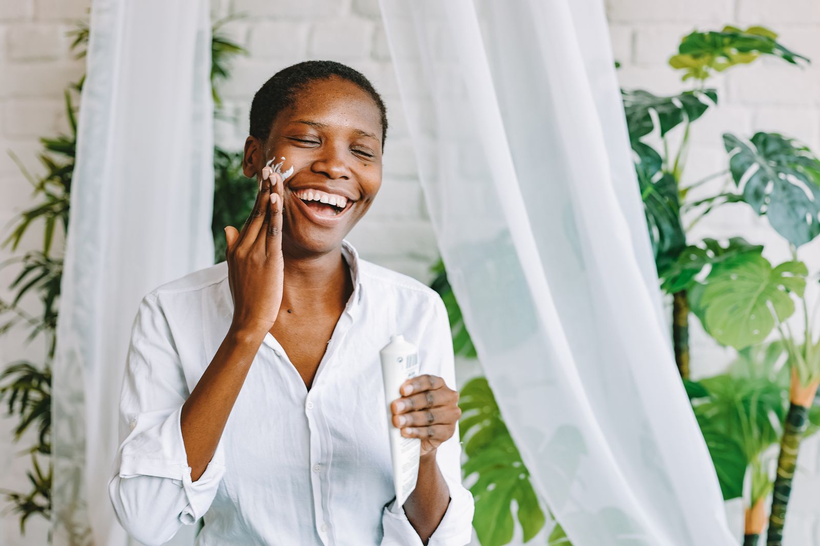 A smiling woman applying face cream in a bright room