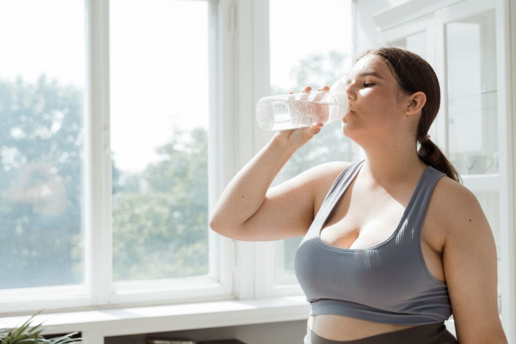 A woman in sportswear drinking water indoors after training