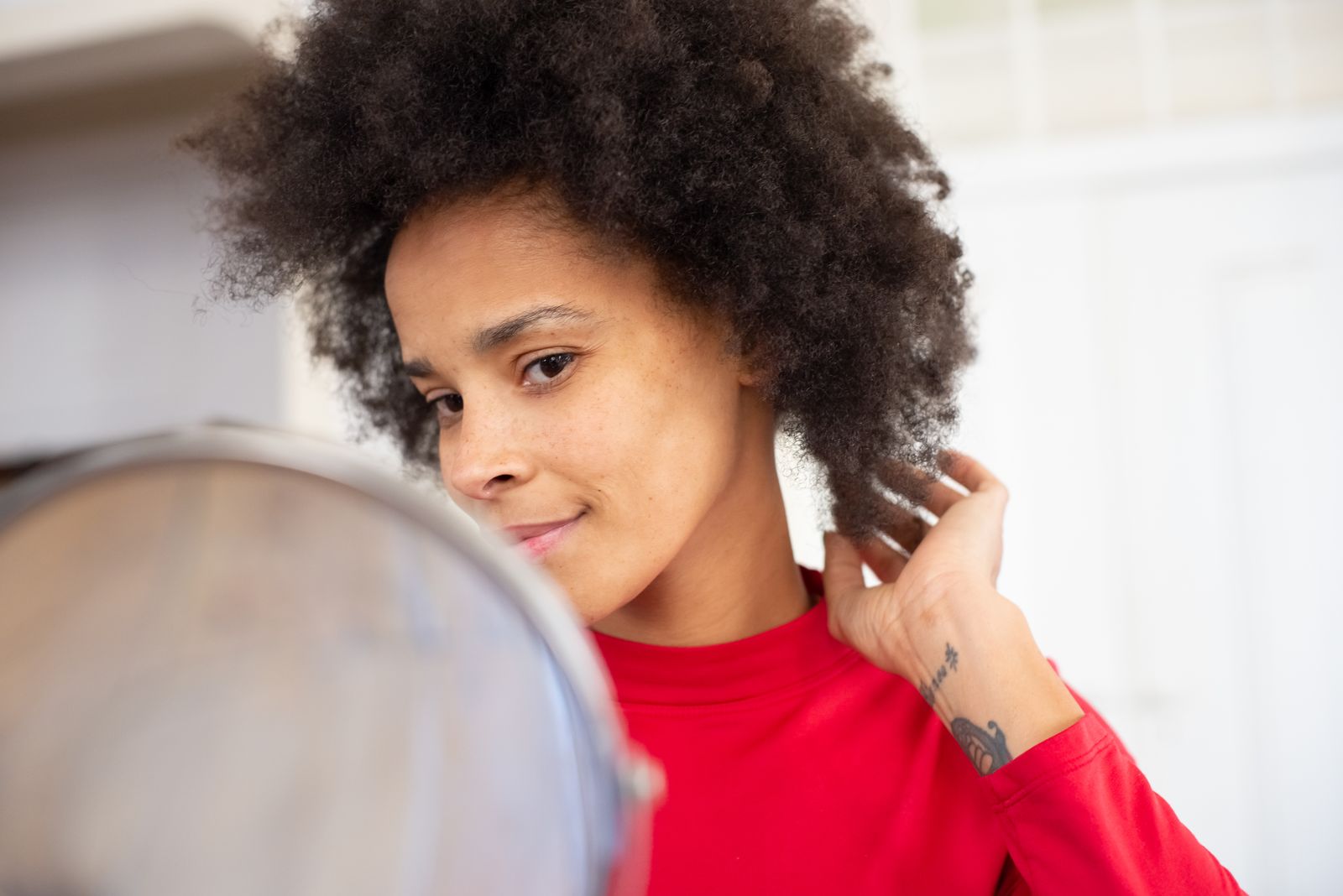 A woman with an afro adjusting her hair in front of a mirror