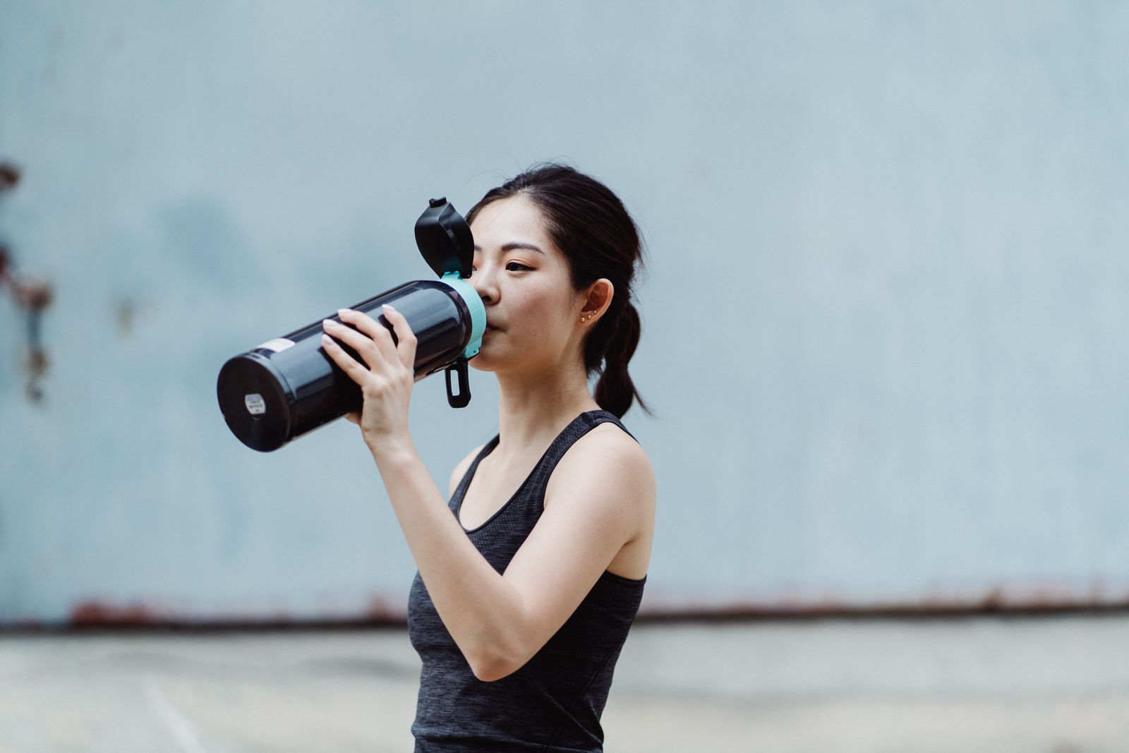 A woman drinking from a bottle while exercising outdoors