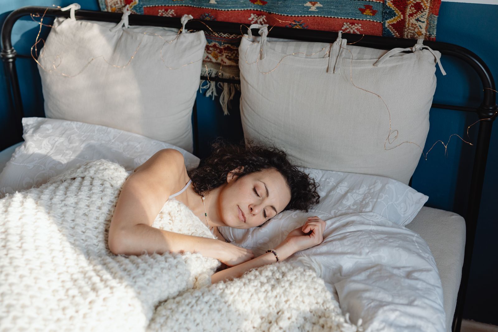 A woman with curly hair asleep under a knitted blanket