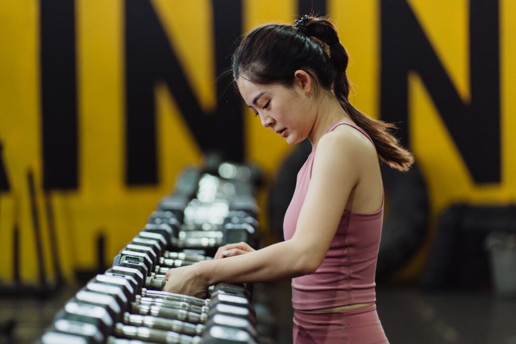 A woman selecting a dumbbell from a rack in a gym
