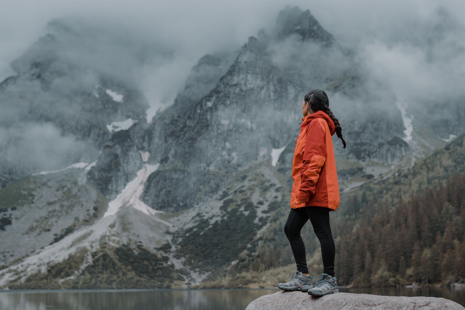 A woman in an orange jacket hiking through a misty mountain landscape