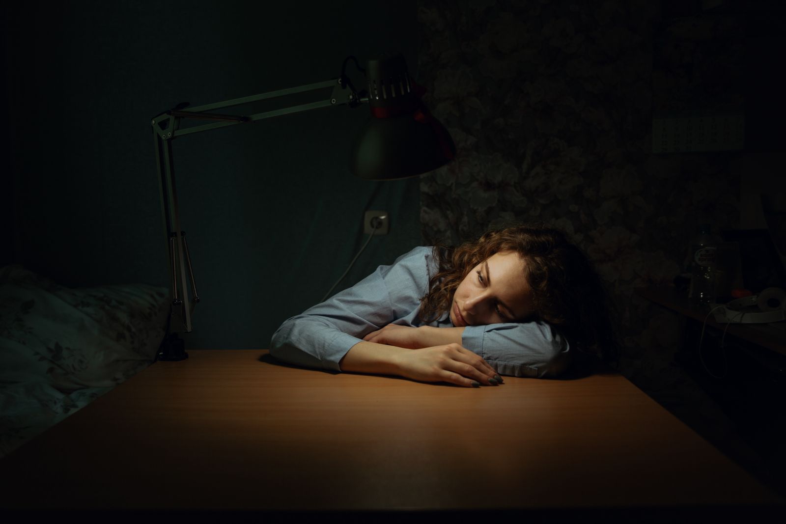 A woman resting her head on a desk in a dim room