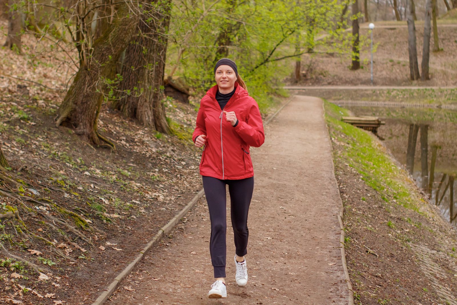 A woman jogging through a forest park in the early morning sunshine