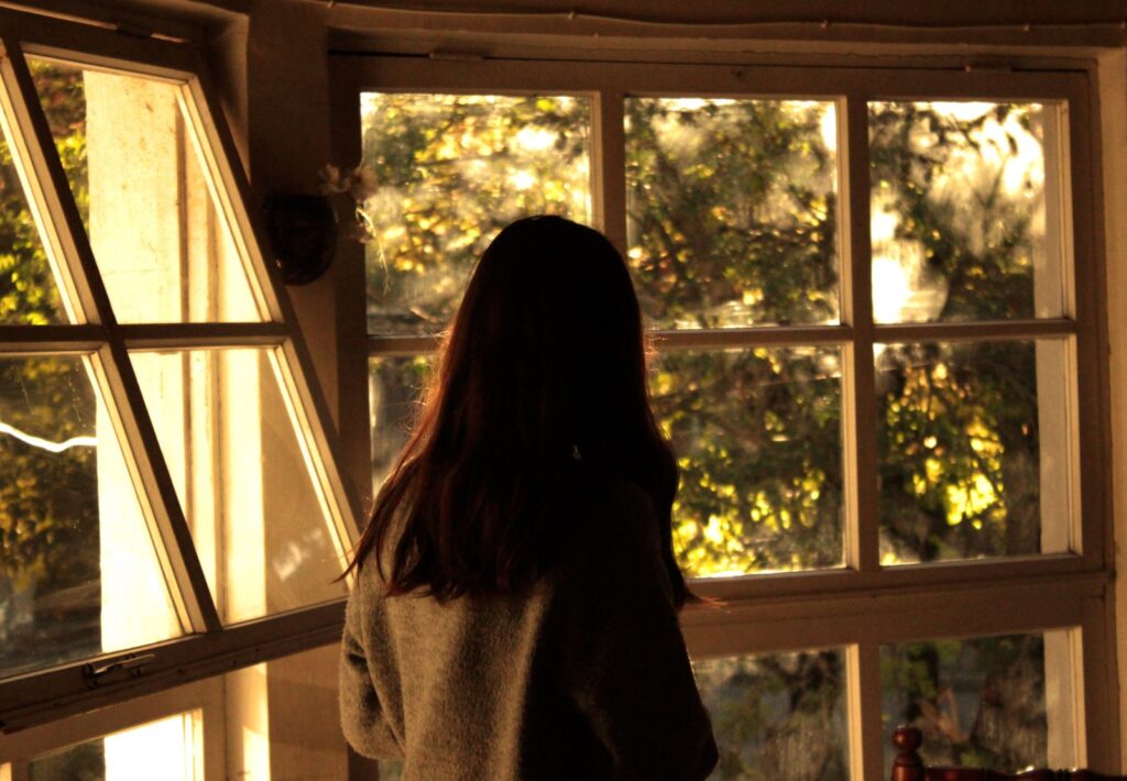 A woman looking out of a window as daylight filters in