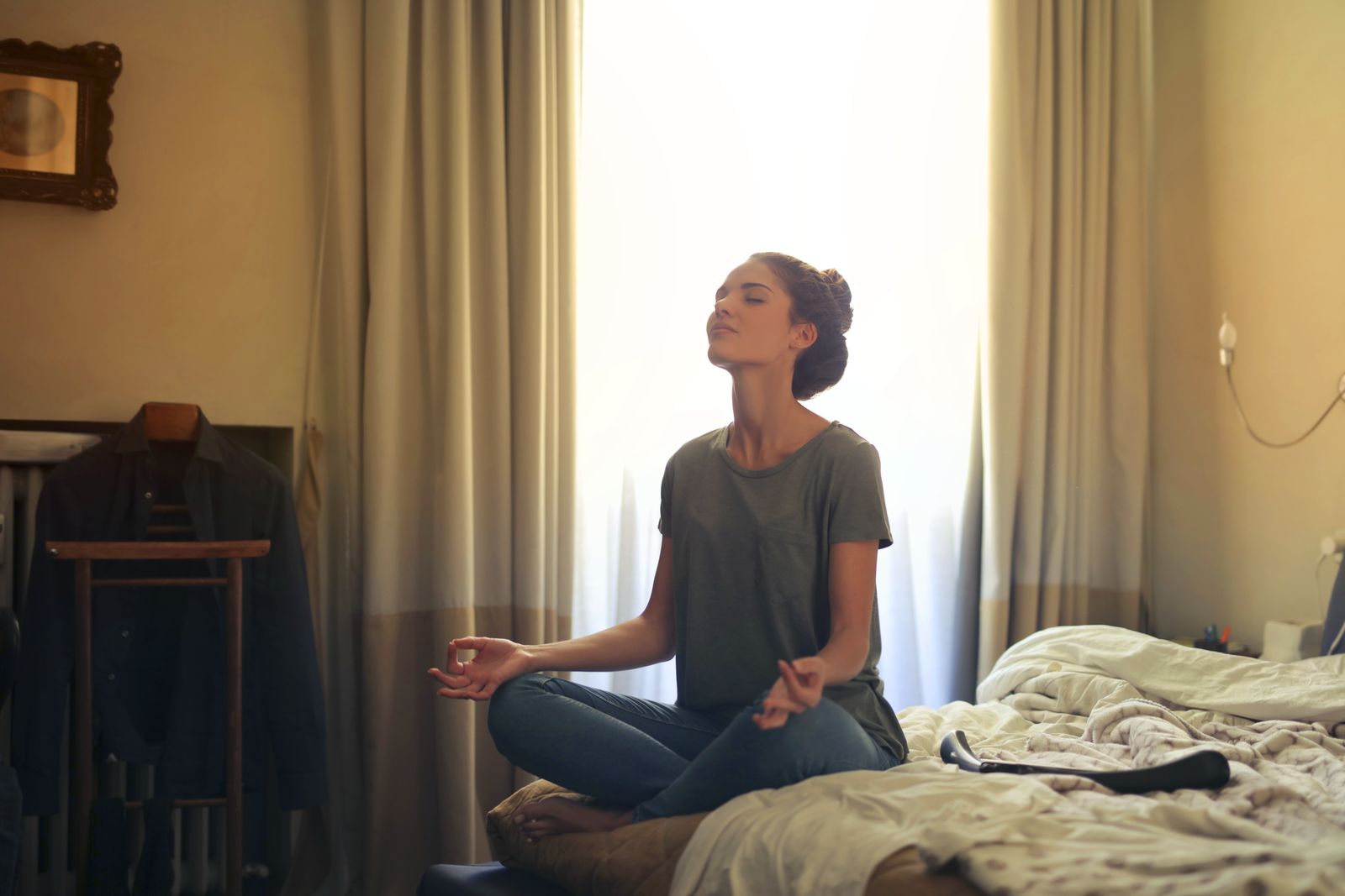 A woman meditating on her bed in a calm bedroom