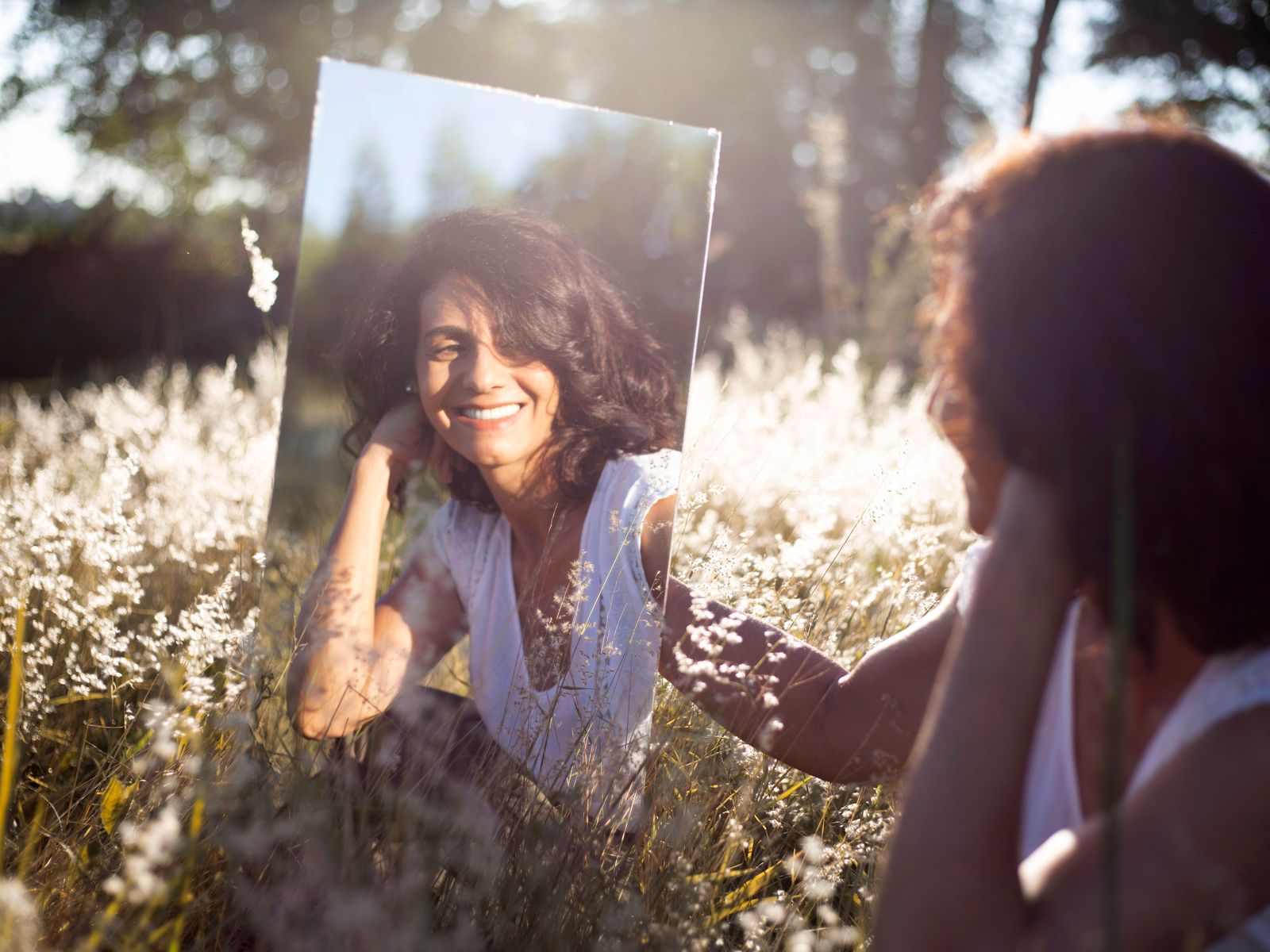 A woman smiling at her reflection in a mirror set in a field