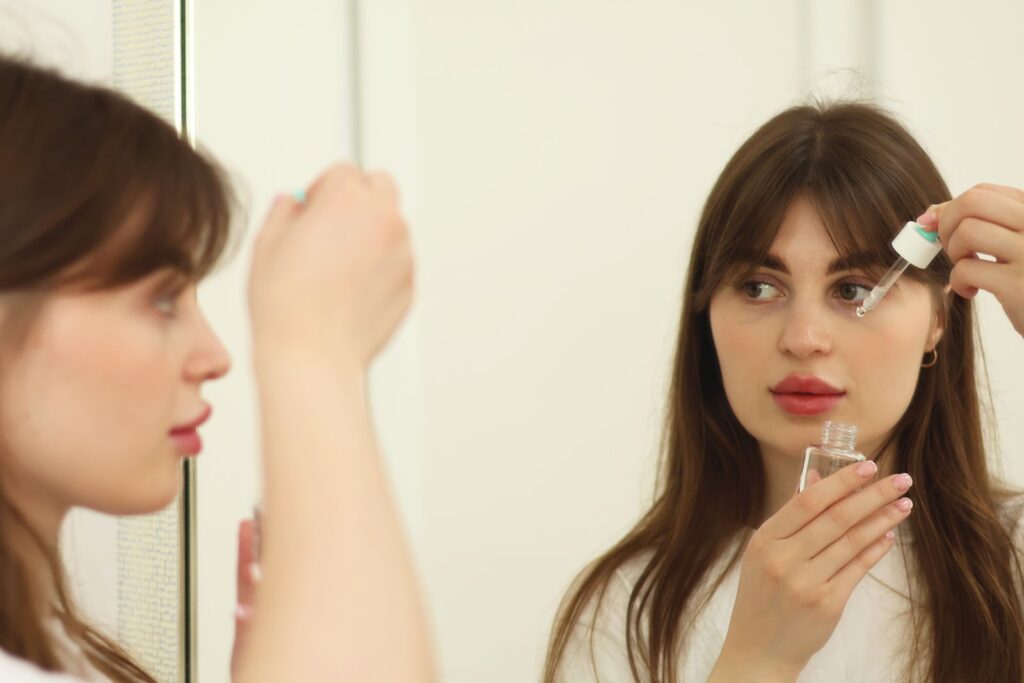 A woman applying a skincare serum in front of a mirror