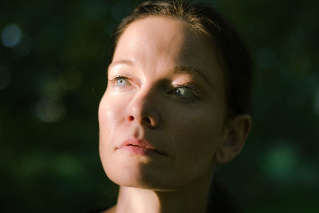 Woman looking upward in a calm outdoor setting with soft daylight