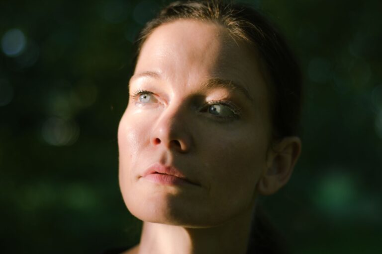 Woman looking upward in a calm outdoor setting with soft daylight