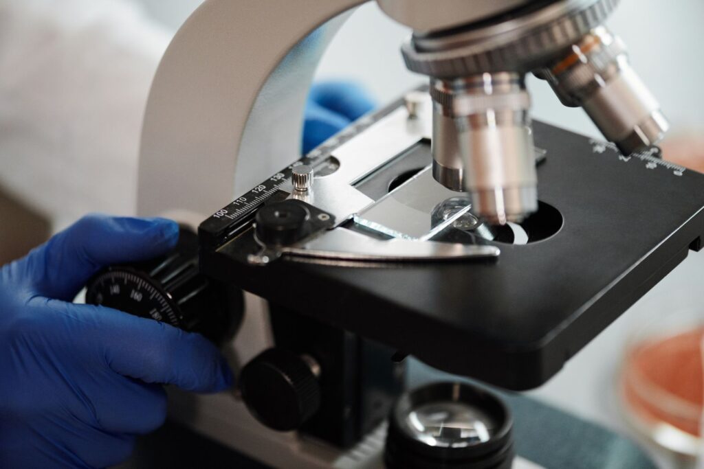 Close-up of a gloved hand adjusting the focus on a laboratory microscope