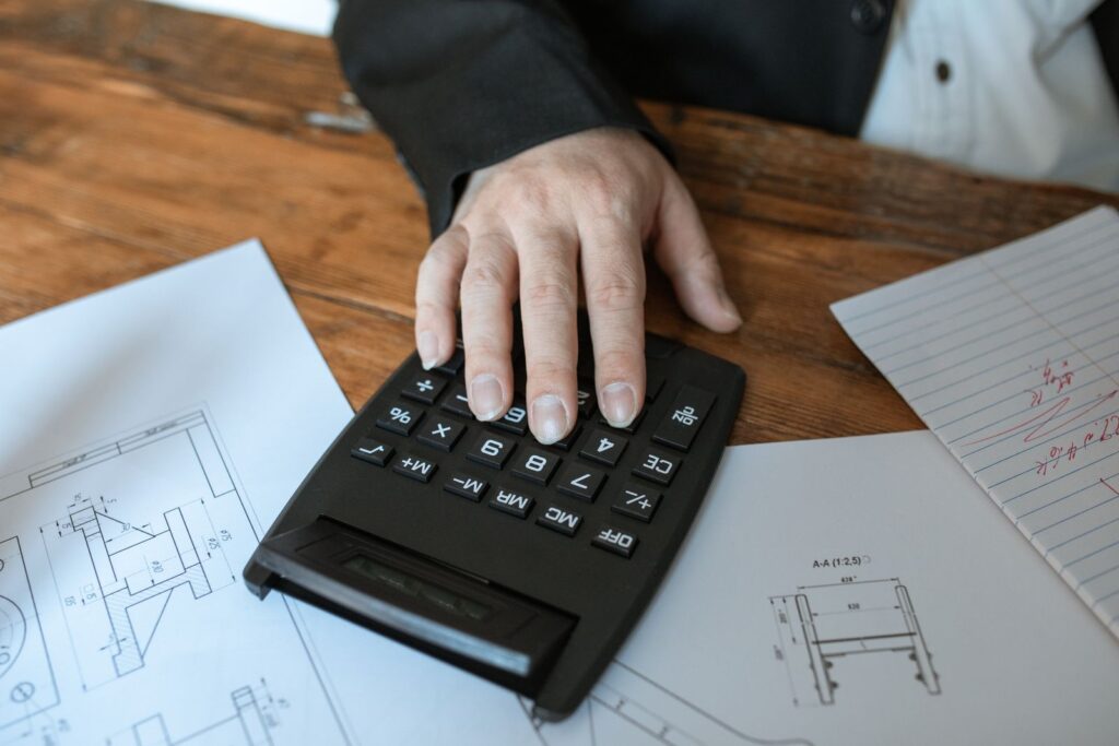A calculator and notebook on a desk beside a laptop